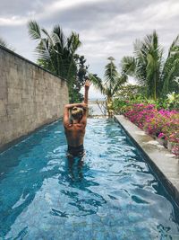 Man in swimming pool by palm trees against sky