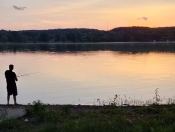 Man fishing in lake against sky during sunset