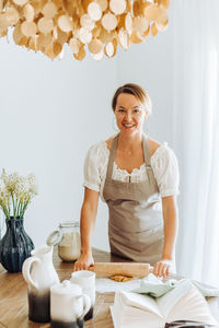 Woman rolling dough for cookies standing at kitchen looking at camera