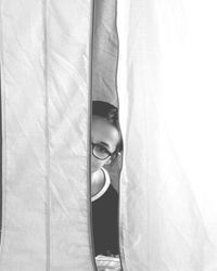 Portrait of young woman hiding behind curtain