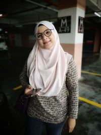 Portrait of mid adult woman wearing hijab using smart phone while standing in parking lot