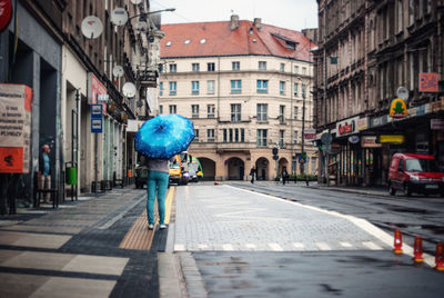 Rear view of woman standing with umbrella on city street