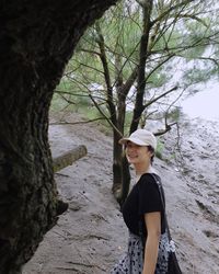 Side view of woman standing by tree trunk