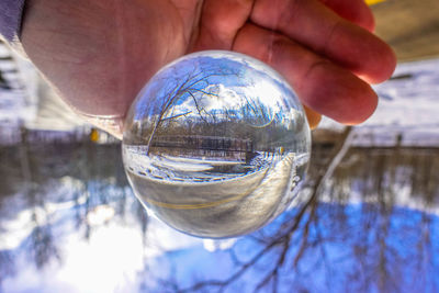 Close-up of hand holding crystal ball with reflection of water