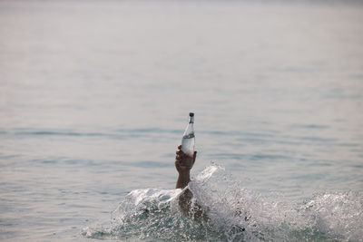 Cropped hand of person holding water bottle in sea