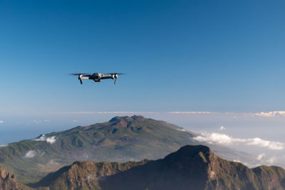 Low angle view of airplane flying over mountains against blue sky