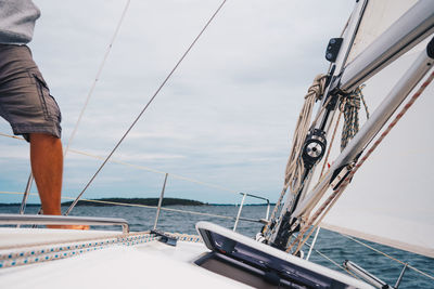 Low section of man standing on sailboat sailing in sea against sky