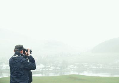 Rear view of man photographing with camera during foggy weather