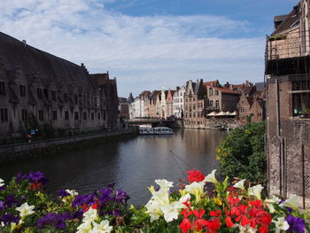 View of buildings by river against cloudy sky