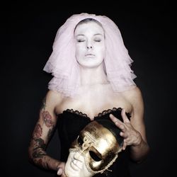 Fashion model with eyes closed holding mask against black background