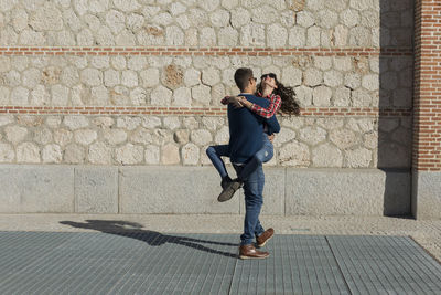 Man lifting happy girlfriend against stone wall