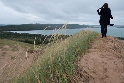 Rear view of woman walking at beach against cloudy sky