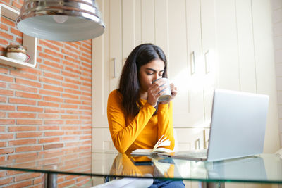 Young woman drinking coffee while sitting in office