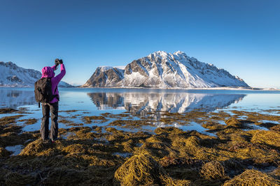 Woman standing on snowcapped mountain against clear sky