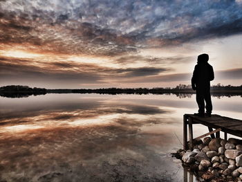 Man standing on lake against sky during sunset