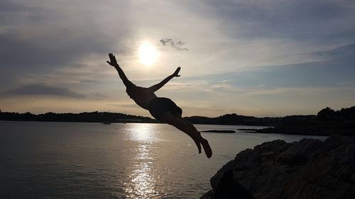 Upside down image of silhouette man on shore against sky during sunset