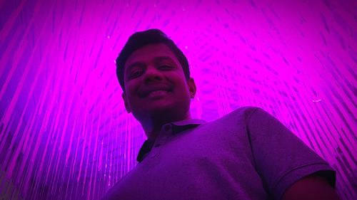 Portrait of young man standing against pink wall