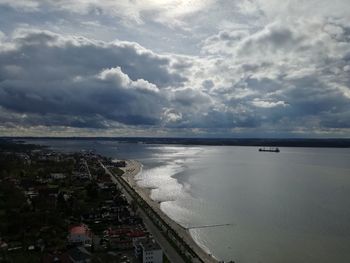 View of city at waterfront against cloudy sky