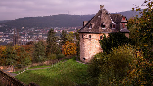 Old house amidst trees and buildings against sky