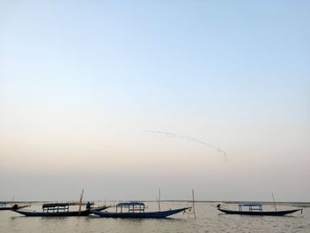 Boats moored in sea against clear sky during sunset