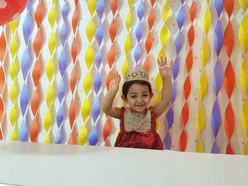 Portrait of smiling girl standing against multi colored curtain