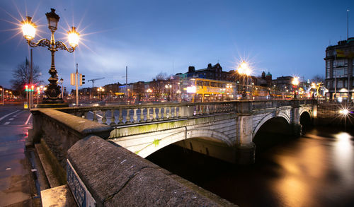 Illuminated bridge over river against sky in city at night
