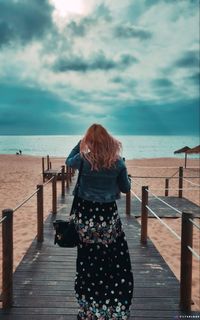 Rear view of woman looking at pier on sea against sky