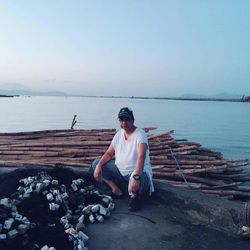 Man sitting on rock by sea against clear sky