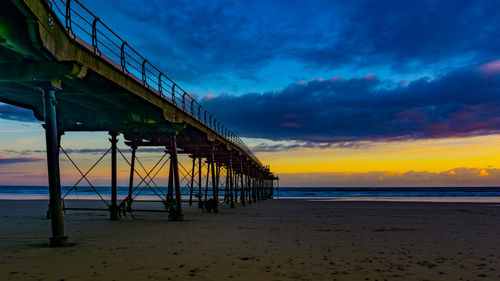 Pier at beach against cloudy sky during sunset
