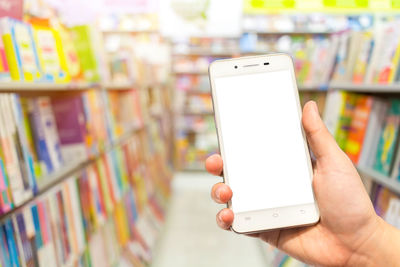 Cropped hand of person using mobile phone against bookshelf in store