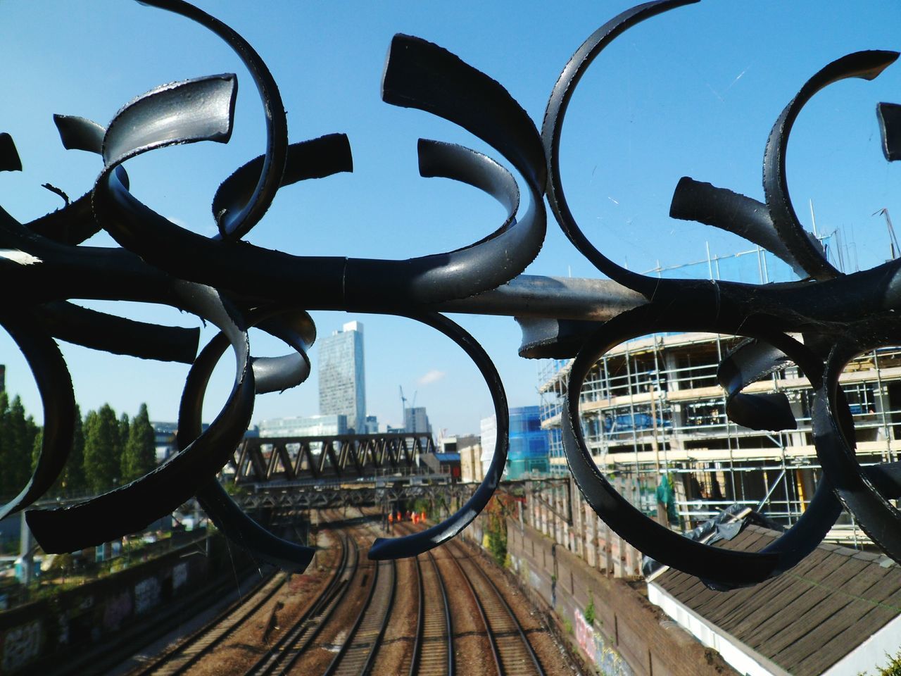 architecture, built structure, transportation, building exterior, clear sky, city, blue, sky, mode of transport, railing, metal, land vehicle, sunlight, outdoors, day, text, bicycle, street, no people, travel