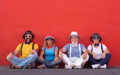 Portrait of cheerful family sitting against red wall