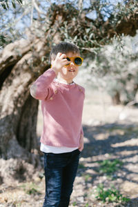 Portrait of boy wearing sunglasses standing against tree