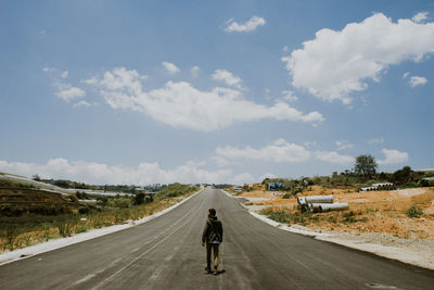 Rear view of man walking on road against sky during sunny day