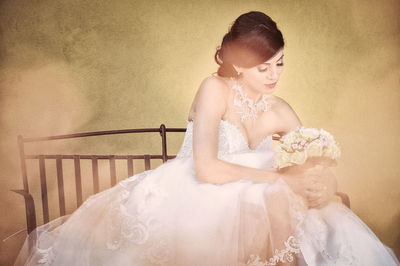 Beautiful young bride with flower bouquet standing against wall