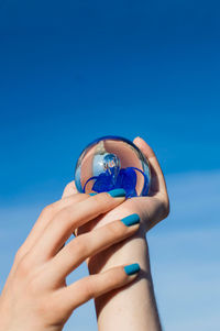 Cropped hands of woman holding crystal ball against blue sky