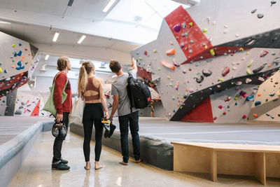 Rear view of man pointing on wall while standing by female and coach in gym