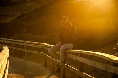 Full length of man sitting on railing during sunset