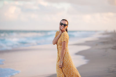 Rear view of woman standing at beach against sky