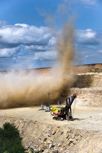 Earth mover on mining mountain against cloudy sky