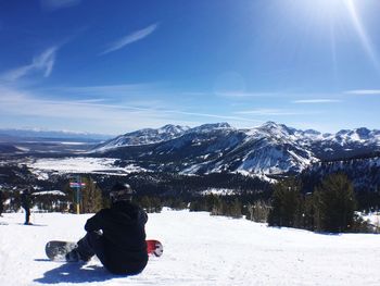Rear view of person with snowboard relaxing on snowcapped mountains