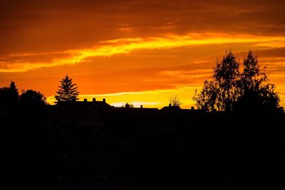 Silhouette trees by house against sky at sunset
