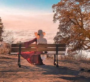 Woman sitting on bench at park during sunset