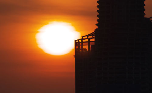 Low angle view of silhouette factory against orange sky