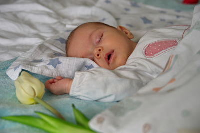 Portrait of cute newborn baby sleeping in bed with tulips around her