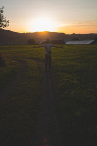 Woman standing on field against sky during sunset