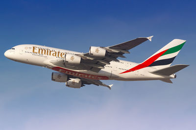 Low angle view of airplane flying against clear blue sky