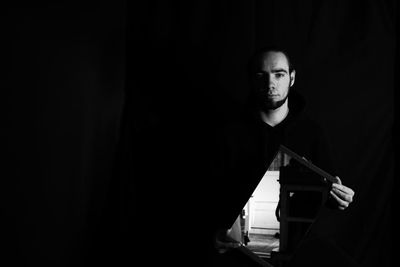 Portrait of man holding mirror standing against black background