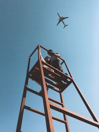 Low angle view of people on lookout tower against clear blue sky
