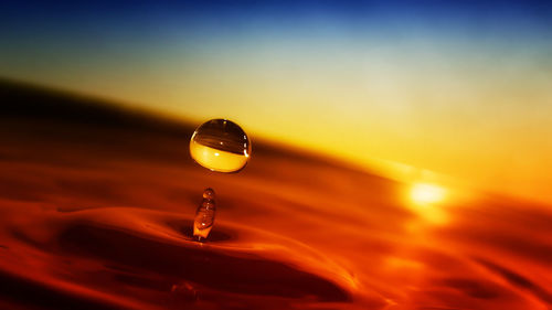 Close-up of water drop against sky during sunset